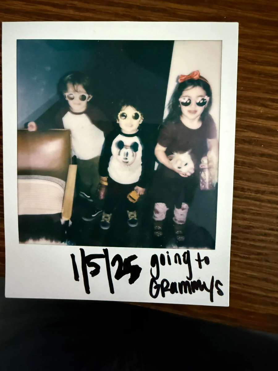 Polaroid photo of three kids wearing sunglasses, standing indoors. One child wears a panda shirt, another has a bow headband, and they all look playful. Text at the bottom says "1/5/25 going to Grammys.
