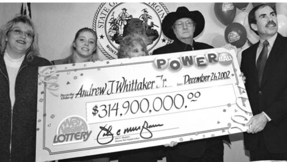A group of people stand holding a giant Powerball check for $314,900,000 made out to Andrew J. Whittaker Jr., dated December 26, 2002. The check displays the West Virginia Lottery logo.
