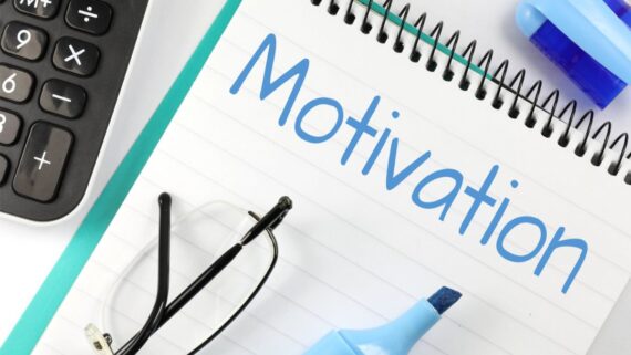 A notebook with the word "Motivation" written in blue, next to a calculator, glasses, and a blue highlighter on a desk.