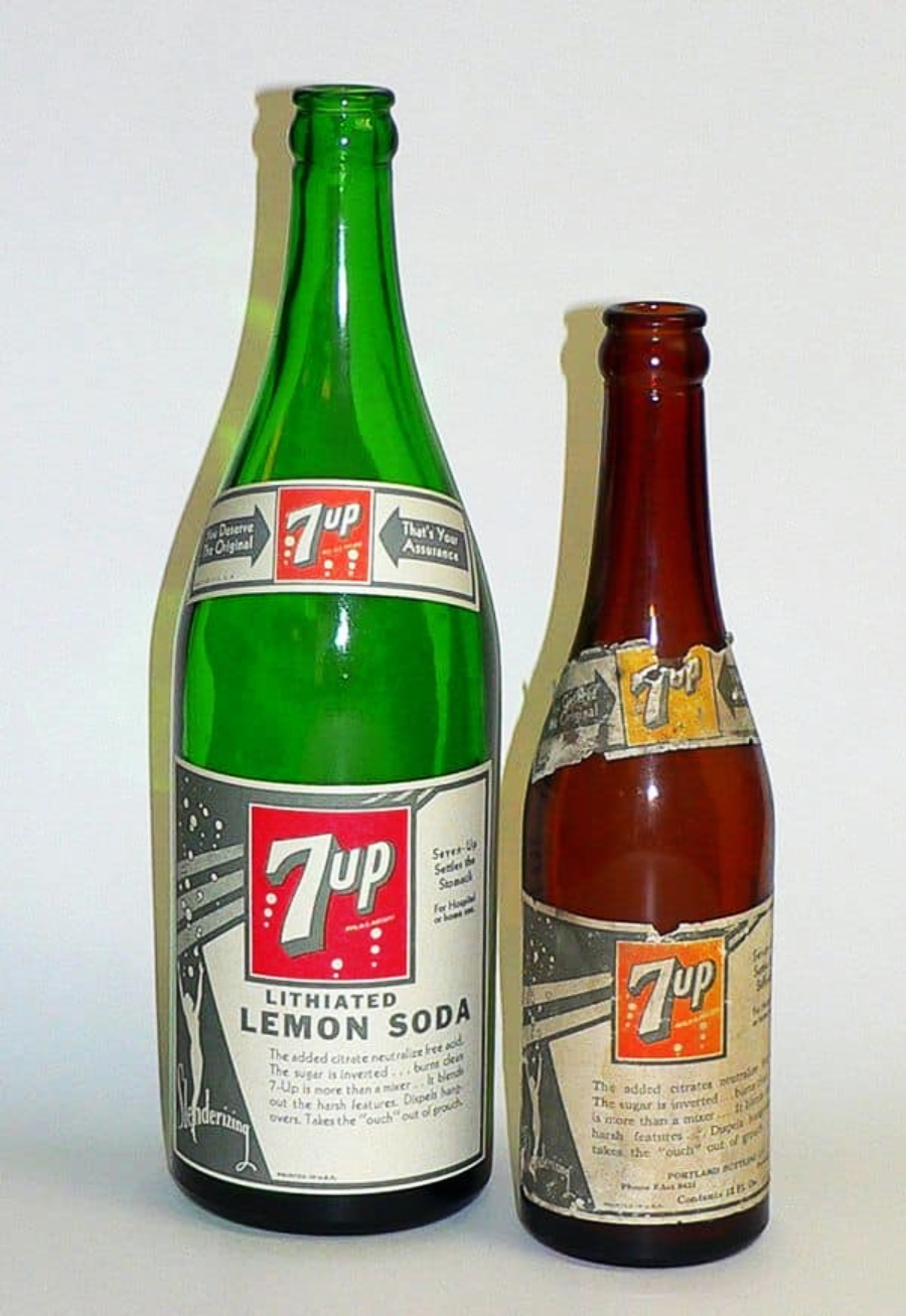 Two vintage 7 Up bottles are shown side by side, one green and one brown, both with old-fashioned labels reading "7 Up Lithiated Lemon Soda." The labels include detailed text and a red 7 Up logo.