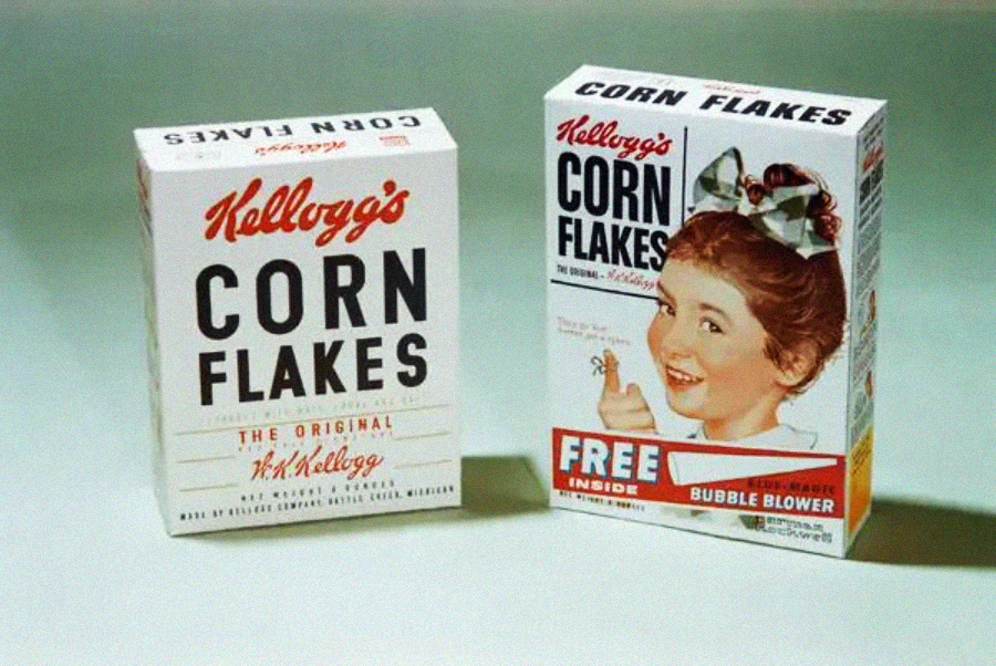Two vintage Kellogg’s Corn Flakes cereal boxes. One features simple text, while the other shows a smiling girl with a bow in her hair and a bubble blower advertisement.