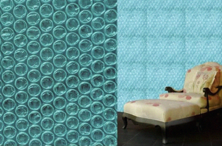 Close-up of blue bubble wrap on the left, transitioning into a wall covered with blue bubble wrap. On the right, a vintage chaise lounge with floral upholstery is positioned against the wall.