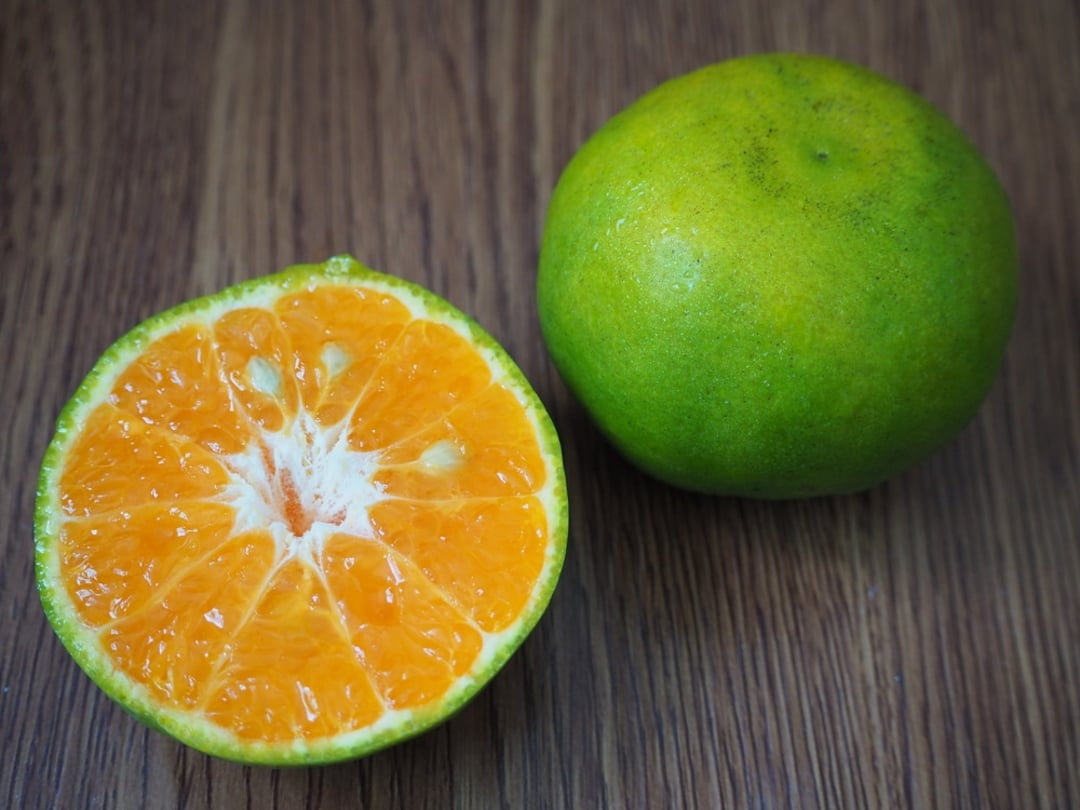 A whole green-skinned tangerine and a half tangerine showing its bright orange, juicy segments, placed on a wooden surface.