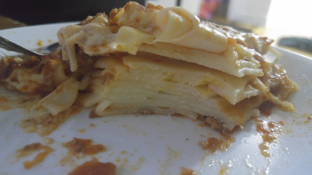 A close-up of a partially eaten slice of lasagna on a white plate, showing distinct layers of pasta, cheese, and sauce.