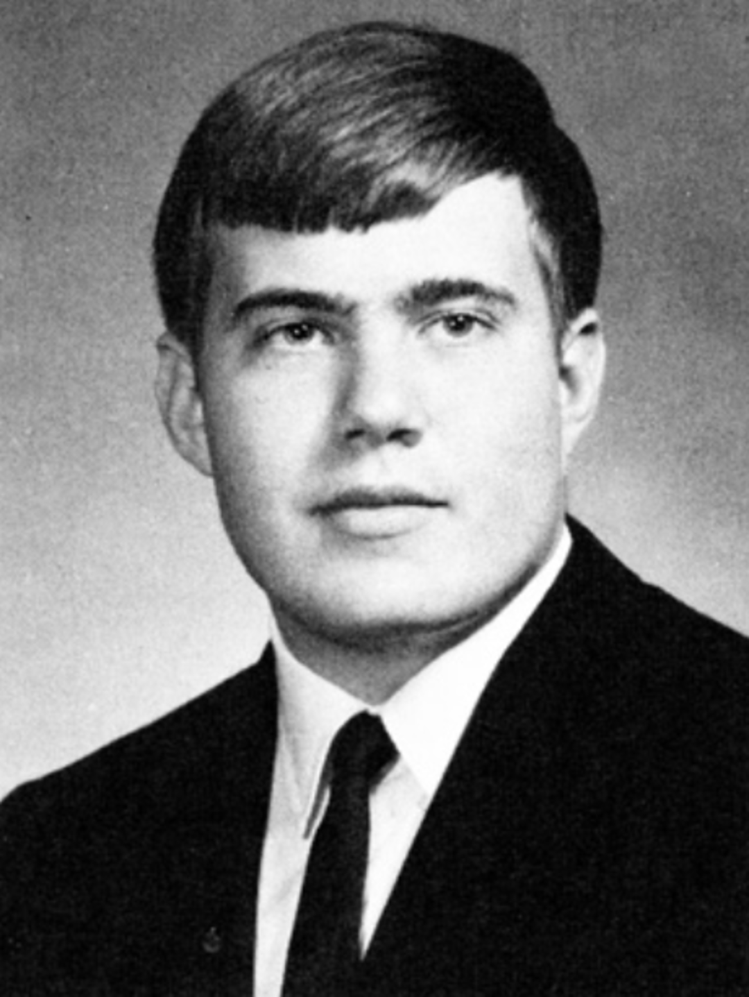 Black and white portrait of a young man in a suit and tie, with short, neatly combed hair, posing against a plain background.