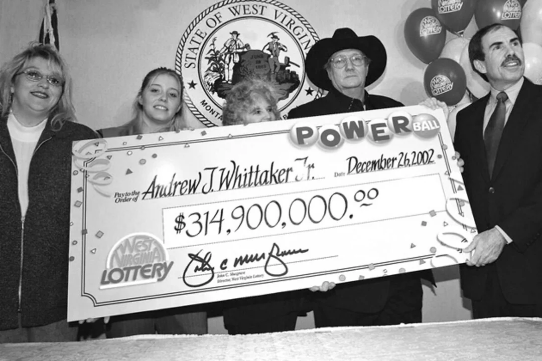 A group of five people holds a large ceremonial Powerball check for $314,900,000 made out to Andrew J. Whittaker Jr. dated December 26, 2002, with "West Virginia Lottery" and state seal in the background.
