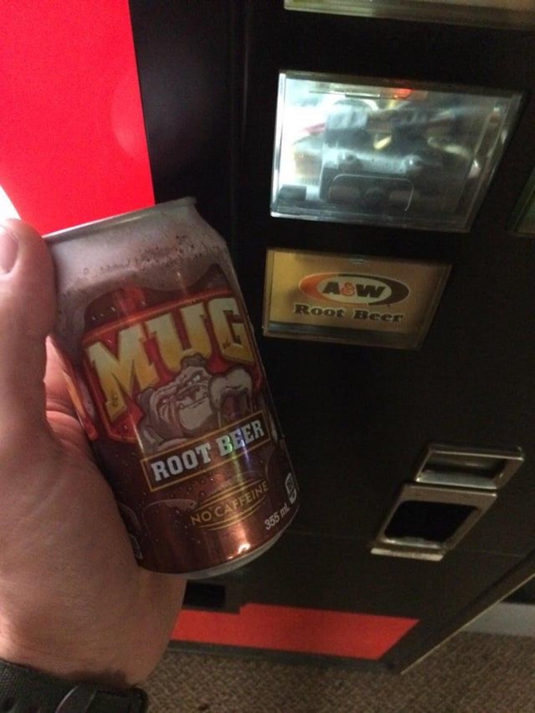 A hand holds a can of Mug Root Beer in front of a vending machine labeled for A&W Root Beer, showing a mix-up between the product received and the advertised option.
