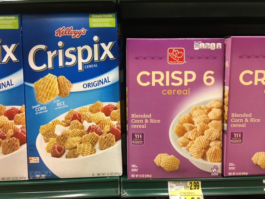 Boxes of Kellogg’s Crispix cereal and a generic brand called Crisp 6 are displayed side by side on a store shelf, both showing cereal pieces in bowls with milk and fruit.
