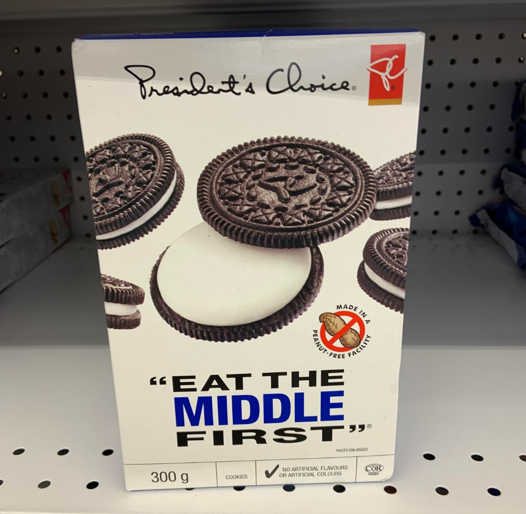 A box of President's Choice cookies resembling Oreos, with the slogan "EAT THE MIDDLE FIRST" and an image showing a cookie with the cream filling exposed. The box is 300g and sits on a store shelf.