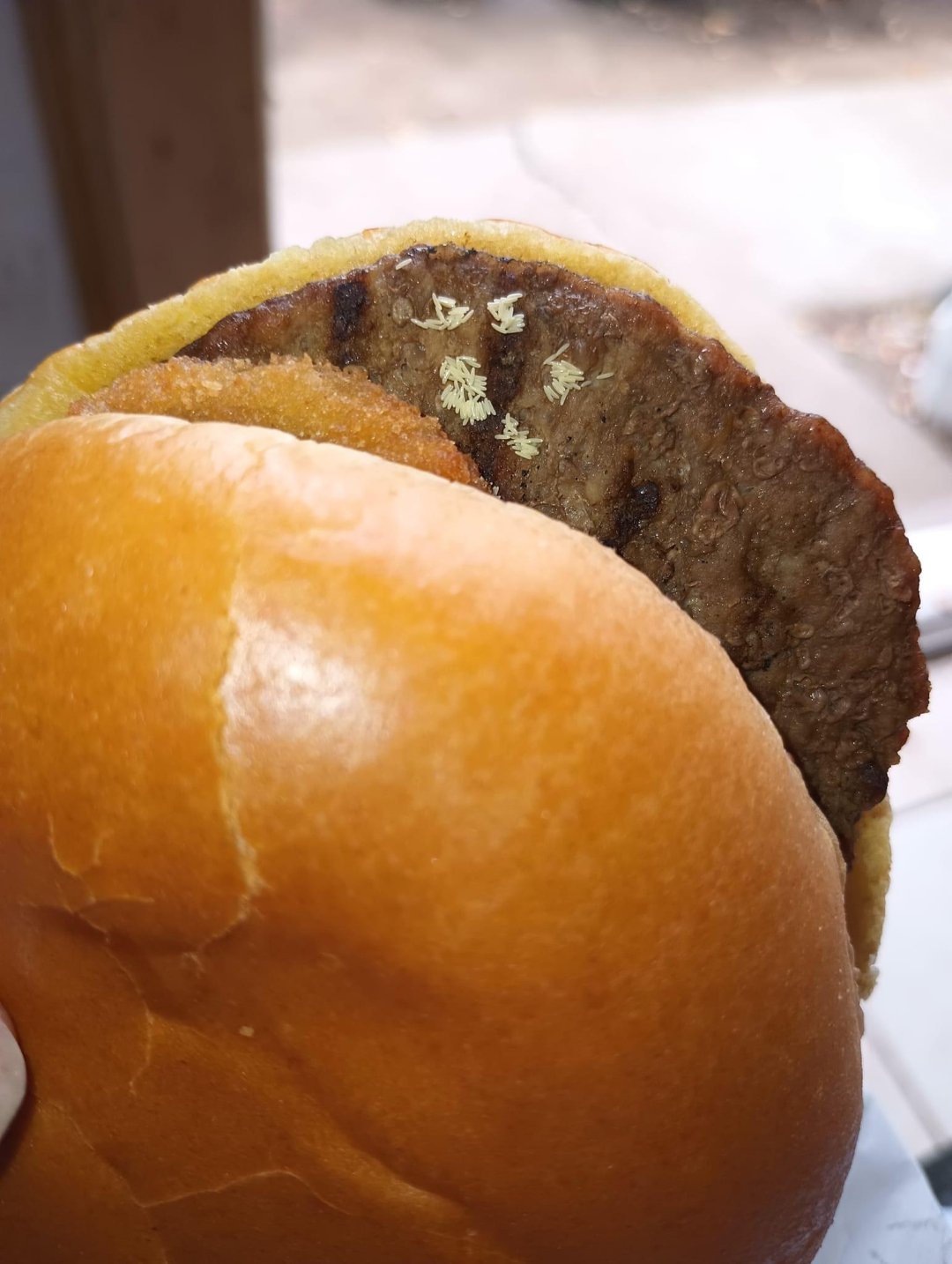 A close-up of a plain hamburger with a beef patty and a soft, shiny bun, shown without any condiments or toppings except for a few small bits of shredded lettuce on the patty.