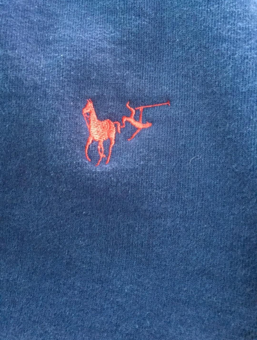 A close-up of a blue fabric with a small red embroidered logo depicting a horse and a polo player holding a mallet.