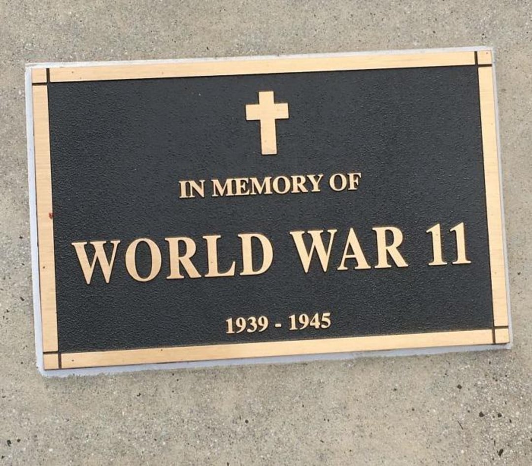 A memorial plaque with a cross reads “IN MEMORY OF WORLD WAR 11, 1939-1945” on a concrete surface. The plaque mistakenly uses "11" instead of "II" for World War II.