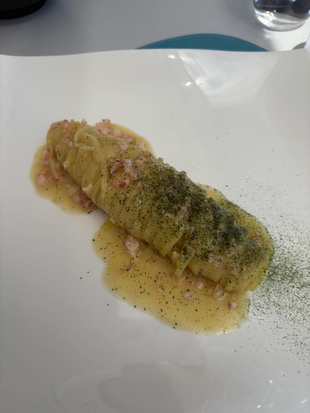 A neatly plated, sliced piece of white fish topped with diced seafood and creamy yellow sauce, garnished with green herbs, is served on a white plate.