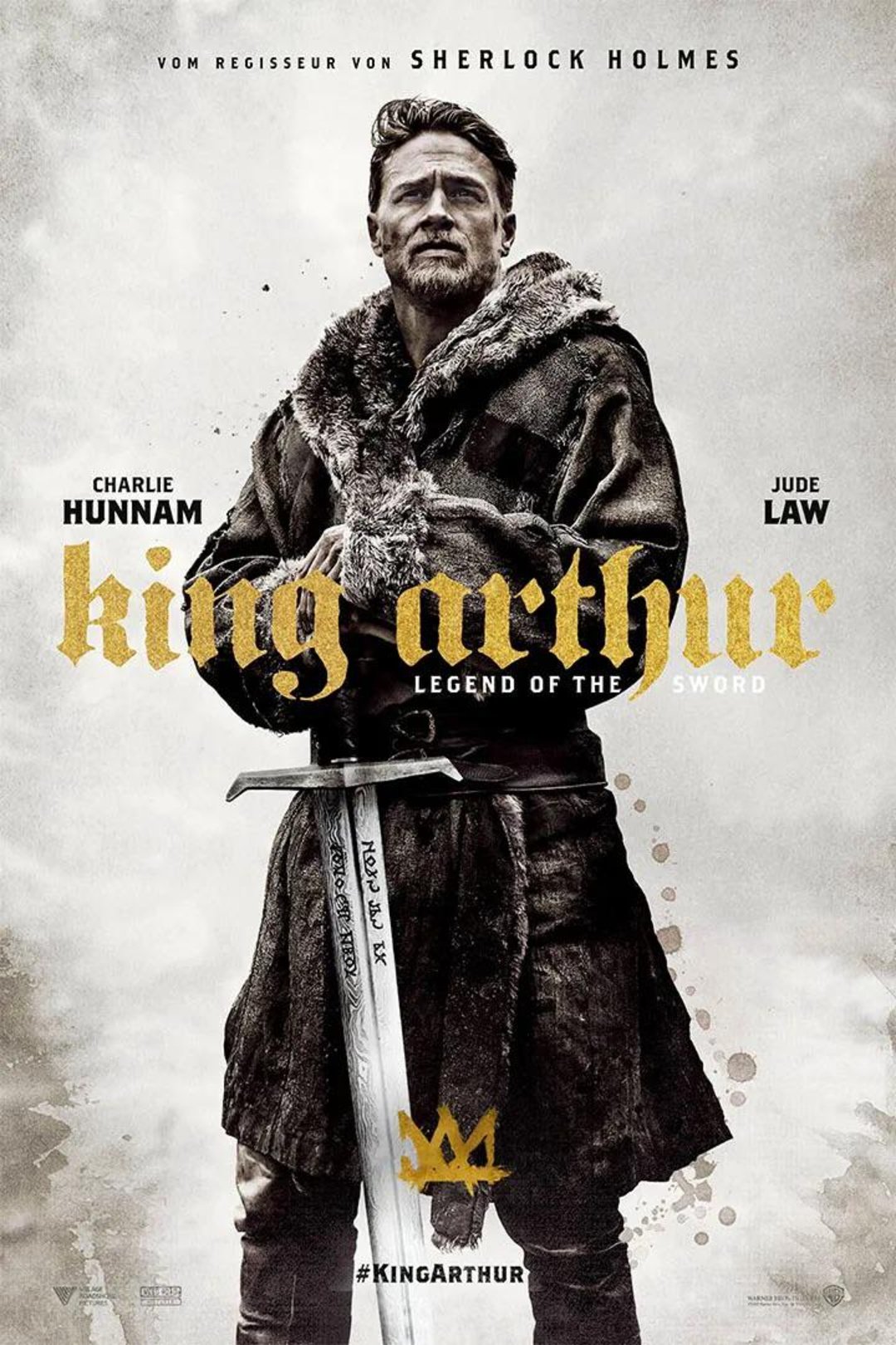 A bearded man wearing medieval clothing holds a sword with both hands, standing against a light background. "King Arthur: Legend of the Sword" is written in gold and white text, with the names Charlie Hunnam and Jude Law above.