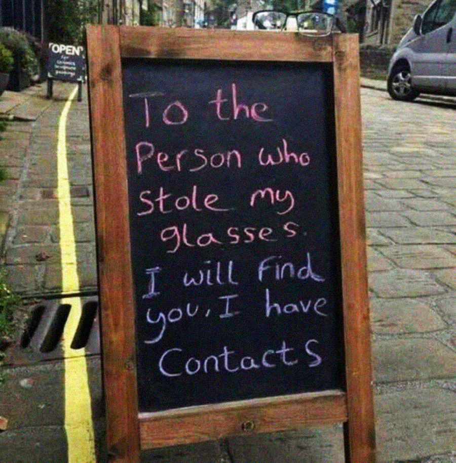 A chalkboard sign on a sidewalk reads: "To the person who stole my glasses. I will find you, I have contacts." The words are written in colorful chalk.