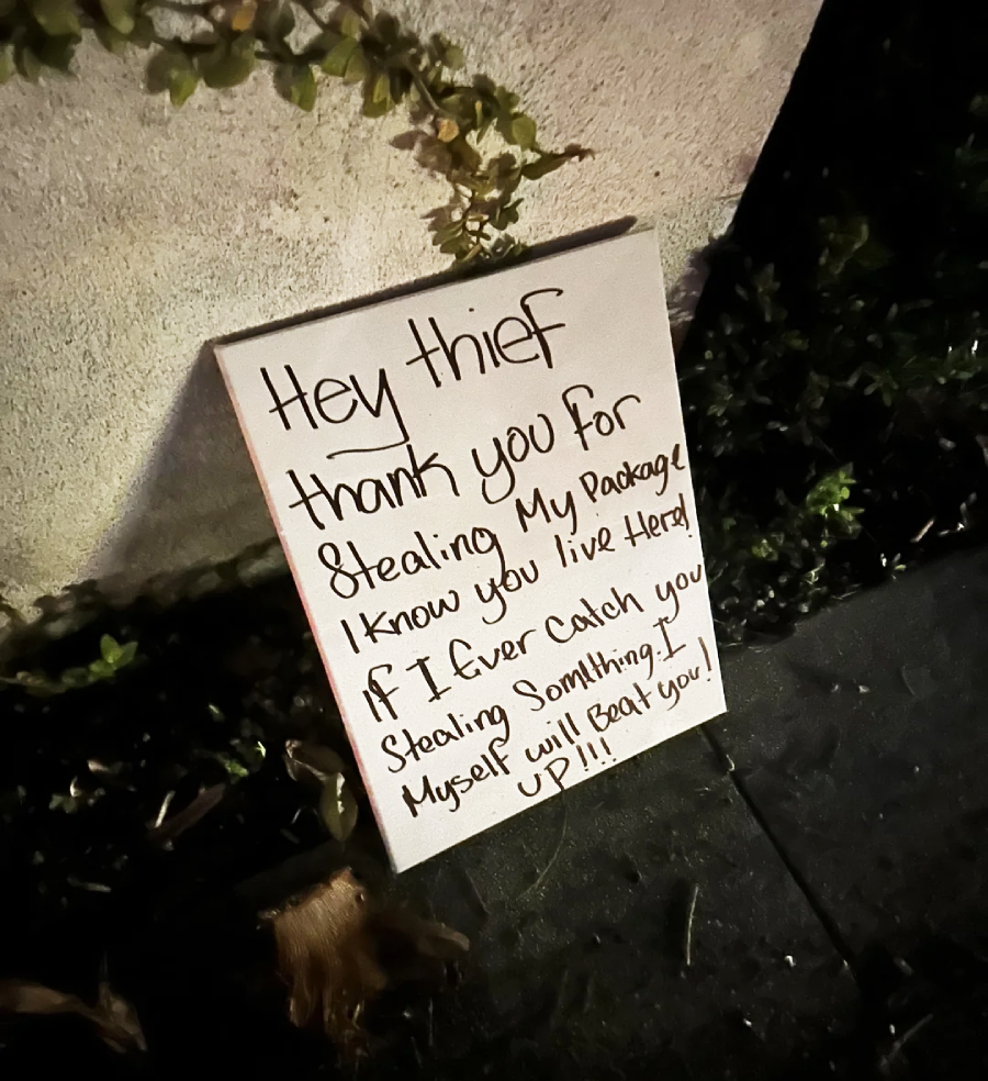 A handwritten sign on the ground reads: "Hey thief, thank you for stealing my package. I know you live here! If I ever catch you stealing something, I myself will beat you up!!!