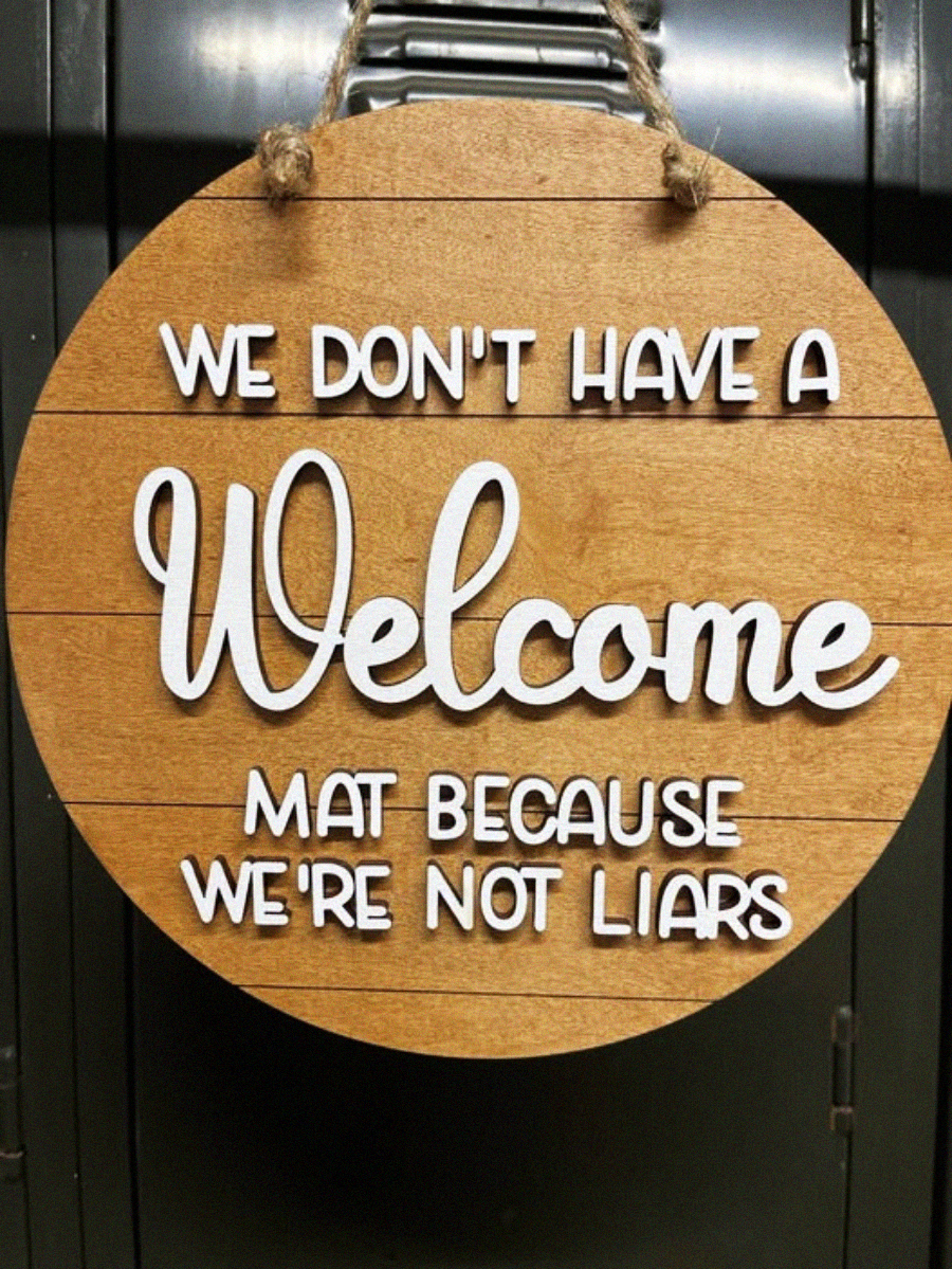 A round wooden sign with white text reads: “We don’t have a welcome mat because we’re not liars.” The sign hangs by a rope.