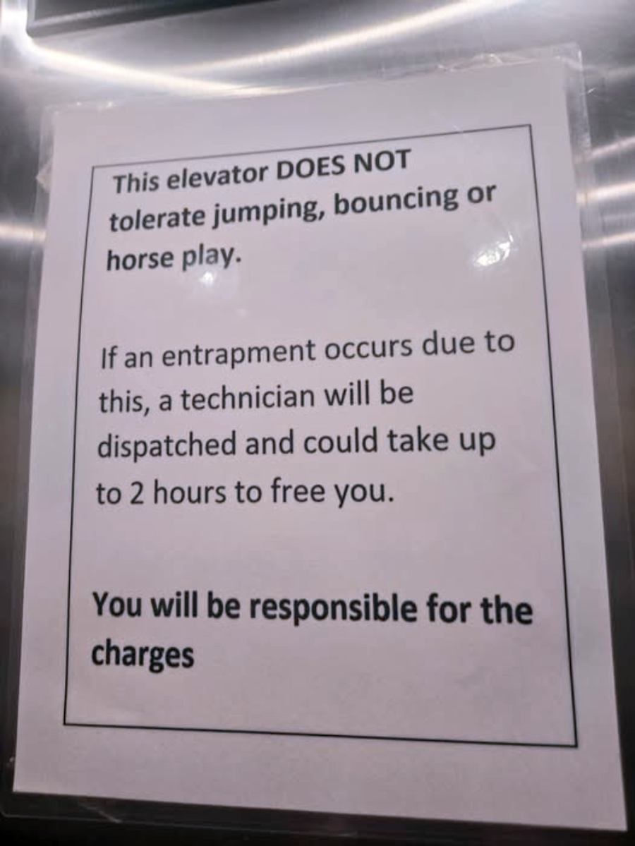 A sign in an elevator warns against jumping, bouncing, or horseplay. It states that entrapment due to such actions may require a technician and up to 2 hours to resolve, with all charges being the passenger’s responsibility.