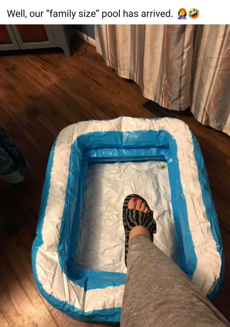 A person with gray pants and zebra-print sandals places a foot inside a small inflatable pool on a wooden floor. The pool is labeled "family size," humorously highlighting its tiny size.
