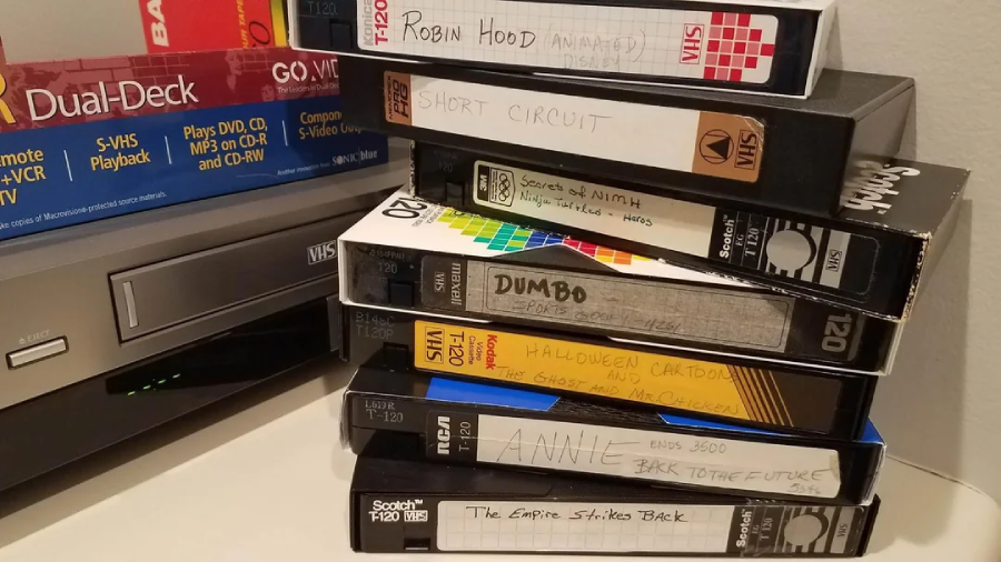 A stack of labeled VHS tapes sits next to a VCR. Visible tape titles include "Robin Hood Animated," "Short Circuit," "Dumbo," "Annie," "Back to the Future," and "The Empire Strikes Back.