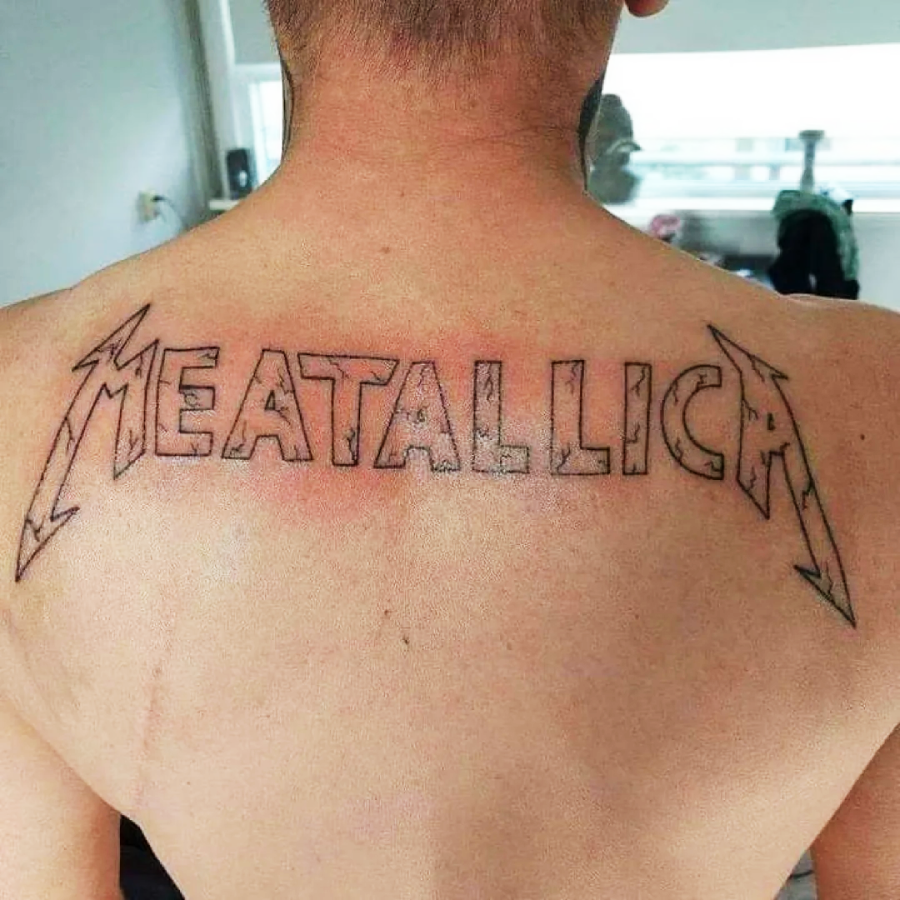 A person with a large back tattoo showing the word "MEATALLICA" in the style of the Metallica logo, with only the outline completed.