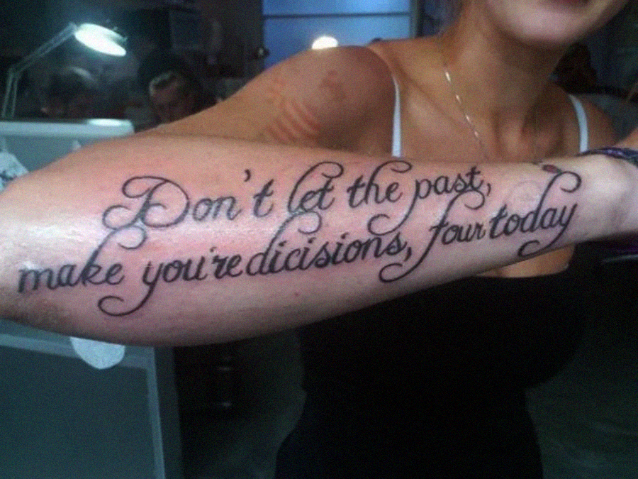 A person displays a forearm tattoo in cursive script that reads, "Don't let the past, make you're dicisions, for today." The tattoo contains spelling errors.