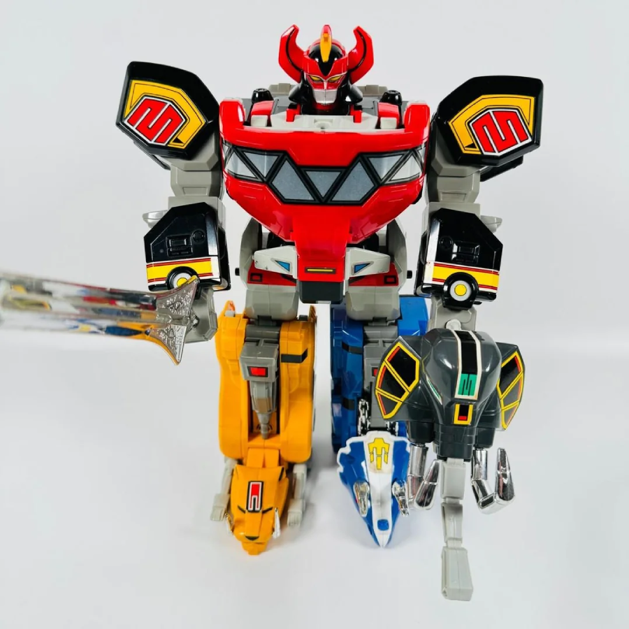 A toy robot combining parts of cars and animals stands upright, featuring bold red, yellow, blue, and black colors, a sword in its right hand, and detailed mechanical features on a plain white background.