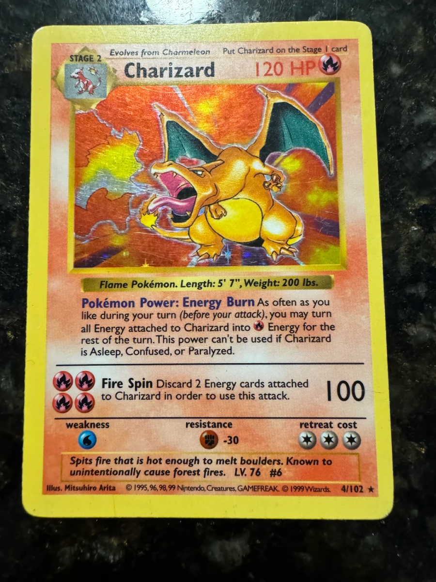 A Charizard Pokémon card with a yellow border, showing Charizard breathing fire with wings spread. The card has 120 HP and features attack and ability details, with a holographic background and visible wear on the edges.