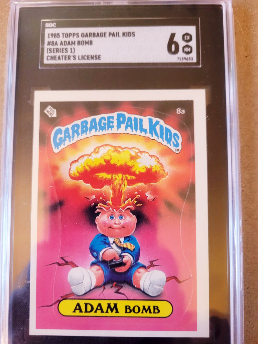 A graded 1985 Topps Garbage Pail Kids trading card showing "Adam Bomb," a cartoon boy with a mushroom cloud explosion coming out of his head. The card is encased in a protective plastic holder.