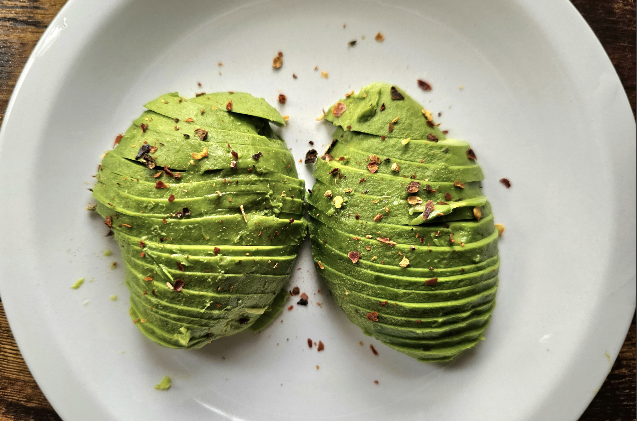 Two halves of a sliced avocado, fanned out on a white plate and sprinkled with red pepper flakes.