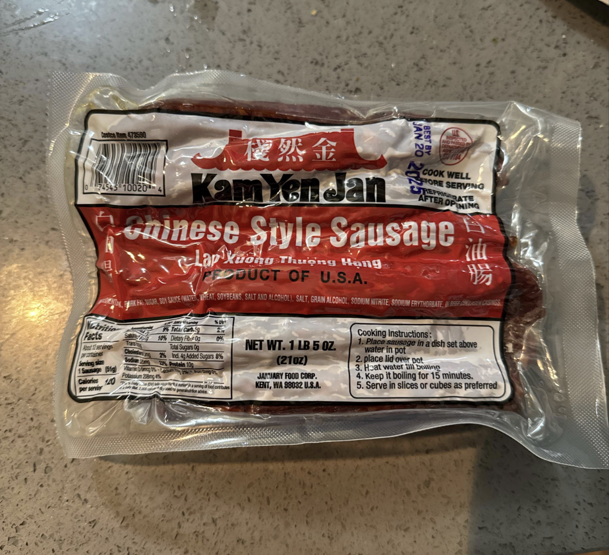 A vacuum-sealed package of Kam Yen Jan Chinese Style Sausage sits on a countertop. The label is mainly red and white with cooking instructions and product details visible.