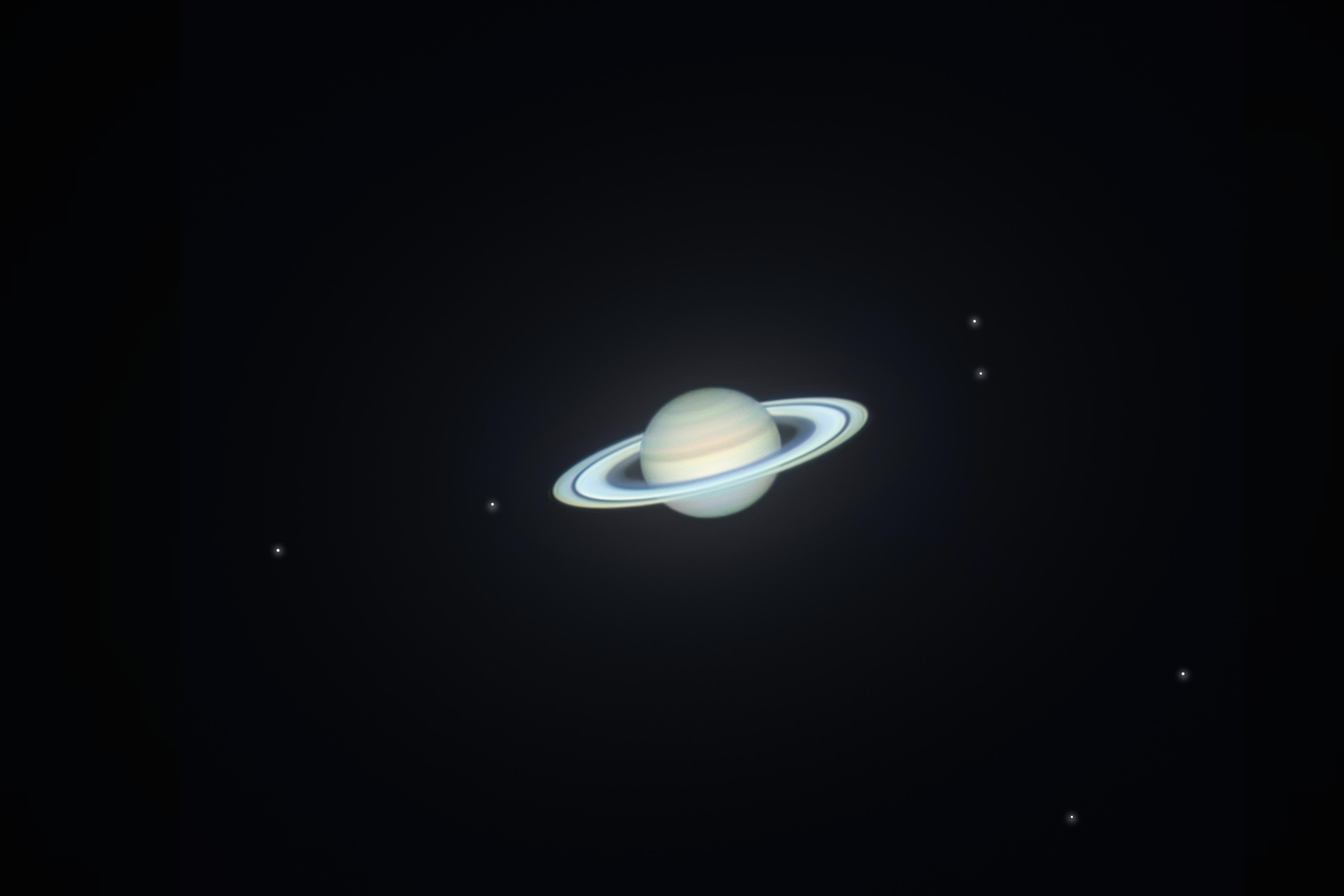 A view of Saturn and its rings set against a dark background, with several small, bright stars scattered around the planet.