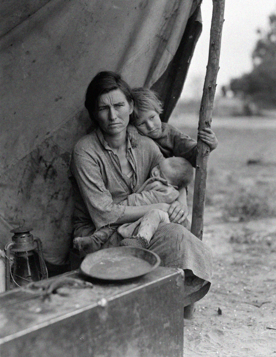A woman sits in front of a tent, holding a baby in her lap while an older child leans on her shoulder. She looks tired and pensive. A lantern and a large plate are on a box nearby in the foreground.