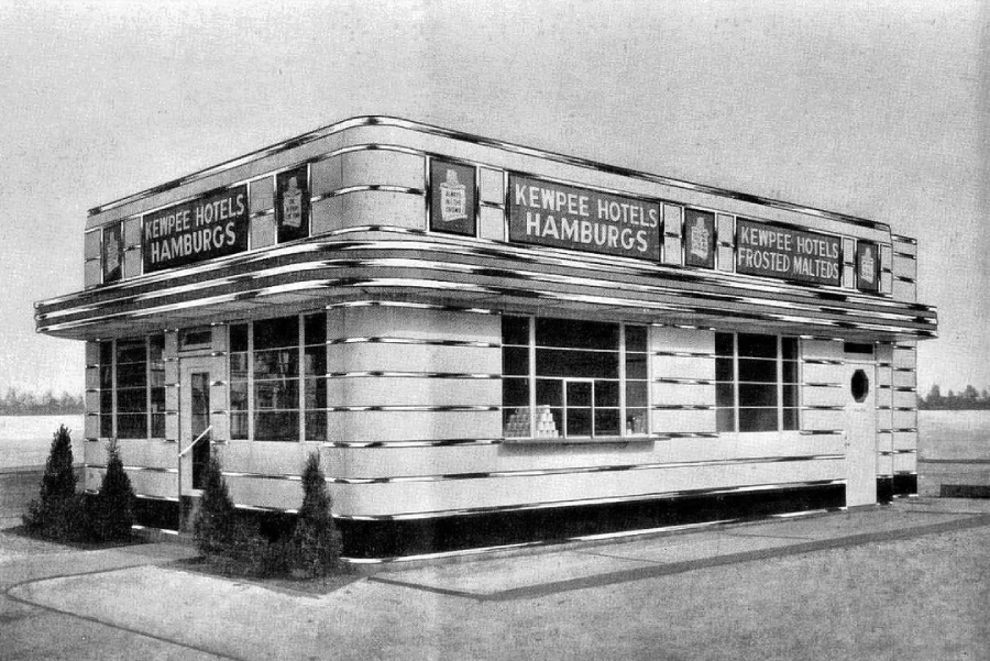 A black and white photo of a vintage diner with art deco styling. Signs read "Kewpee Hotels Hamburgs" and "Kewpee Hotels Frosted Malteds." Bushes line the building’s exterior, and there are large windows and a round door.