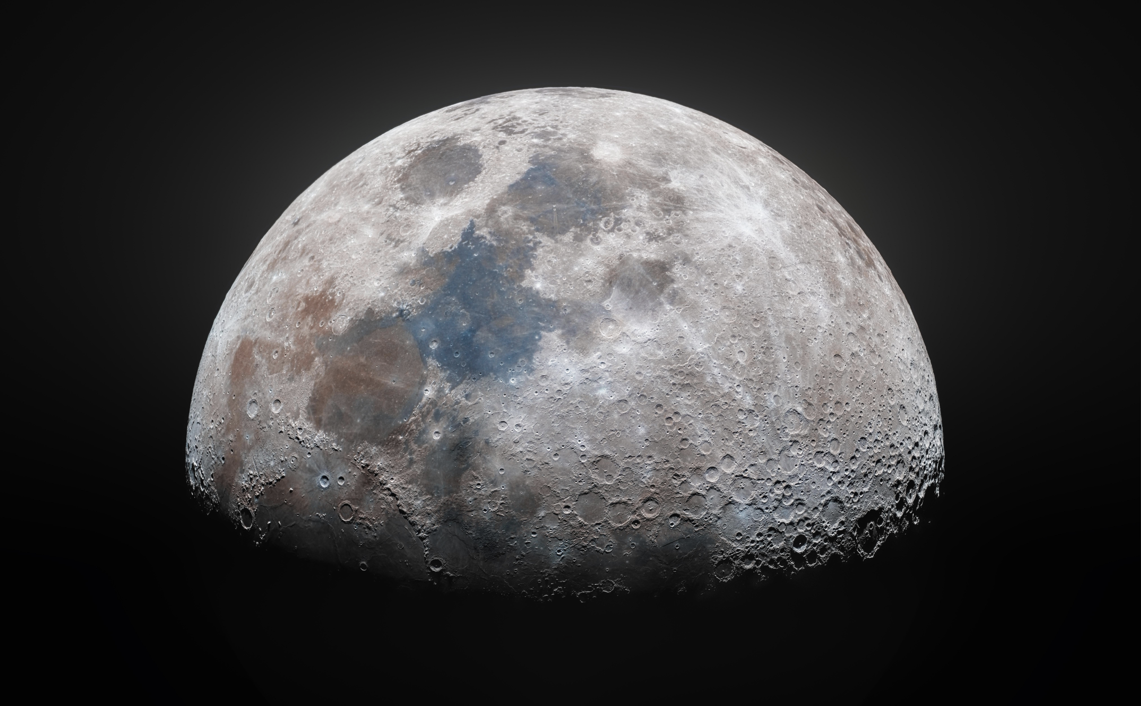 A detailed, color-enhanced image of the moon’s surface showing craters, maria, and highlands, with a dark background highlighting the moon’s lower half and its textured, diverse terrain.