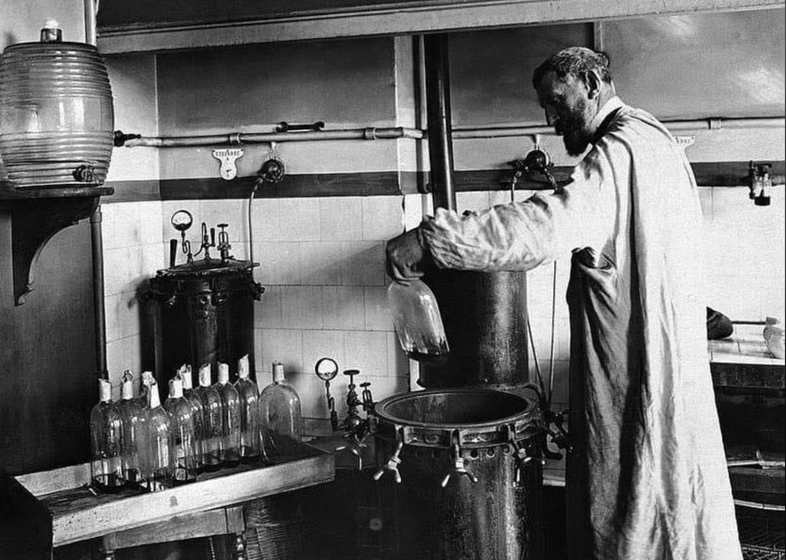 A scientist in a lab coat pours liquid into a glass bottle, surrounded by other bottles and laboratory equipment in an early 20th-century laboratory setting.