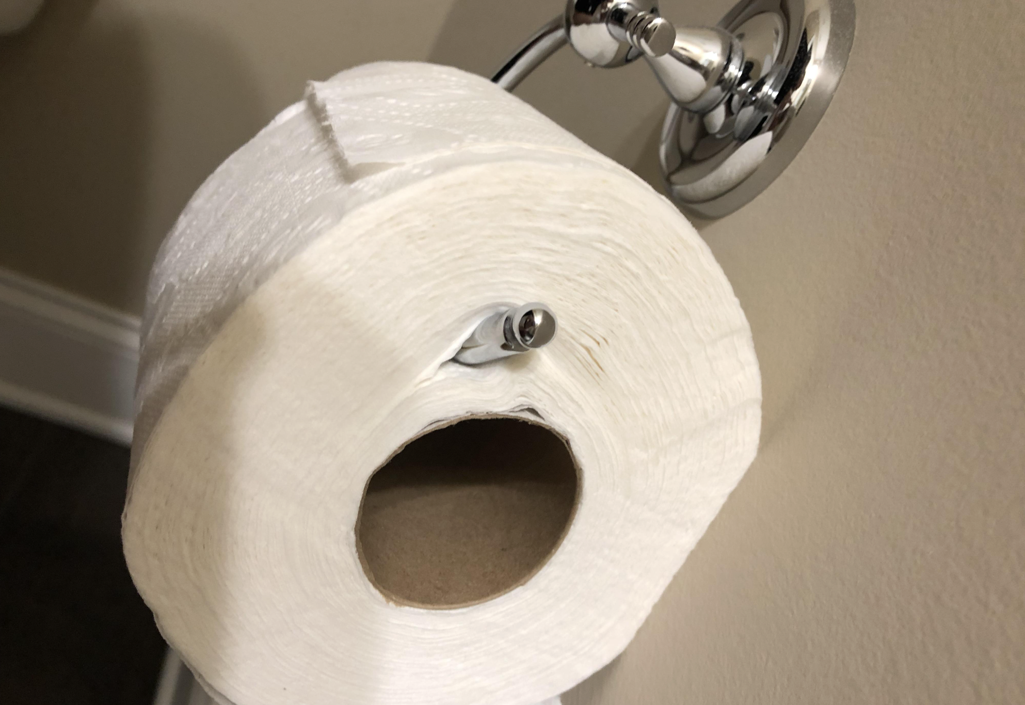A toilet paper roll mounted incorrectly, with the holder rod placed through the paper rather than the cardboard tube, on a wall-mounted holder.