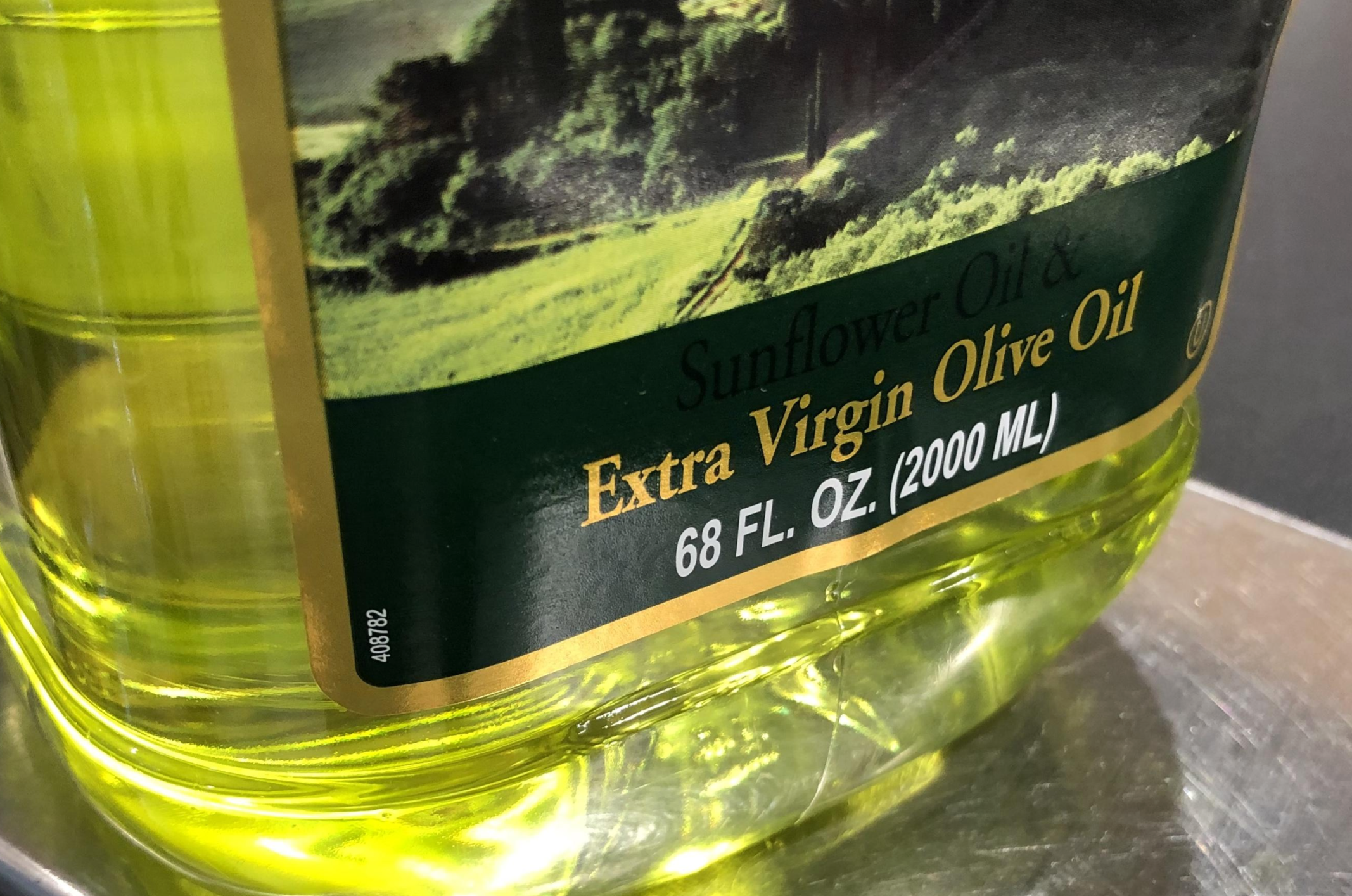 A close-up of a bottle label showing "Sunflower Oil & Extra Virgin Olive Oil, 68 FL. OZ. (2000 ML)" in yellow and green text, with a scenic landscape image above the text.