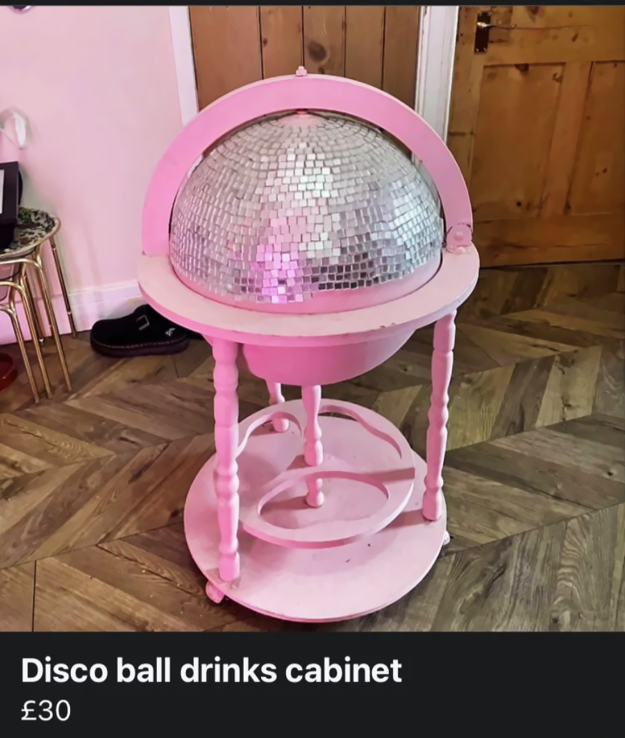 A pink drinks cabinet with a hinged disco ball top, standing on four legs with a lower shelf, placed on a wooden floor near a closed door. Price listed as £30.