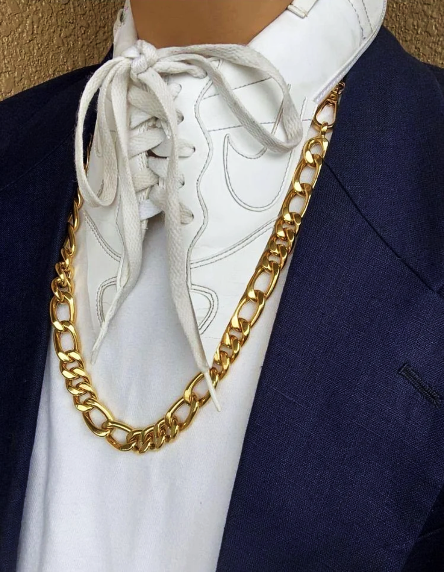 A person wearing a white lace-up shirt with a visible Nike logo, a navy blazer, and a chunky gold chain necklace. Only the neck and upper chest are visible.