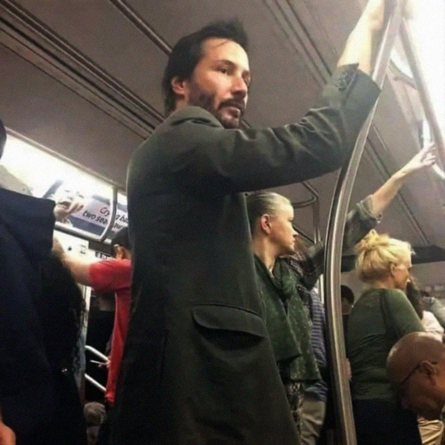 A man in a dark jacket stands and holds a railing inside a crowded subway train, surrounded by other passengers.