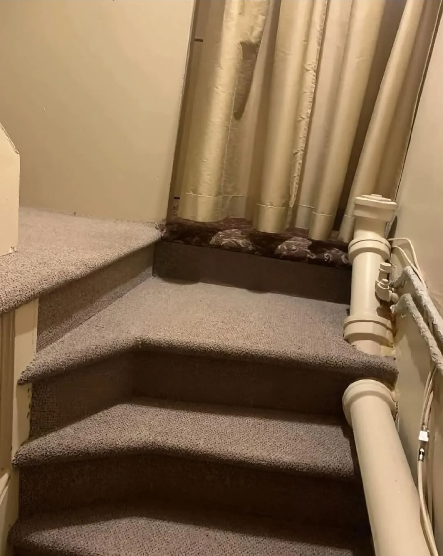 A carpeted staircase leads to a landing blocked by a beige curtain. The curtain hangs down, preventing access to whatever is at the top of the stairs. A railing runs along the right side.