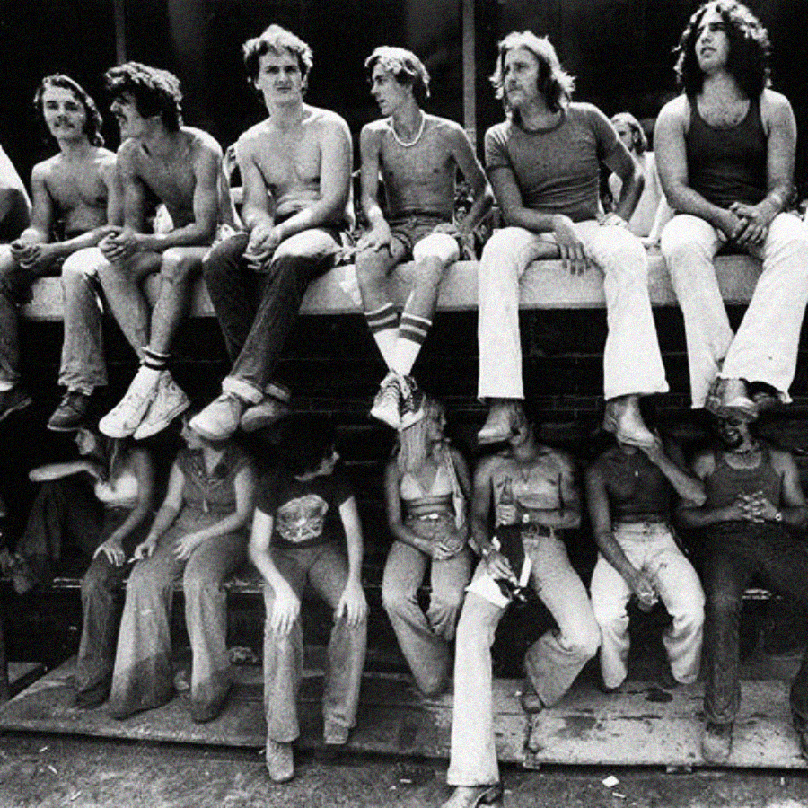 A black-and-white photo shows two rows of young people sitting on a ledge; the upper row appears upright, while the lower row is directly beneath, seemingly upside down, creating an optical illusion.