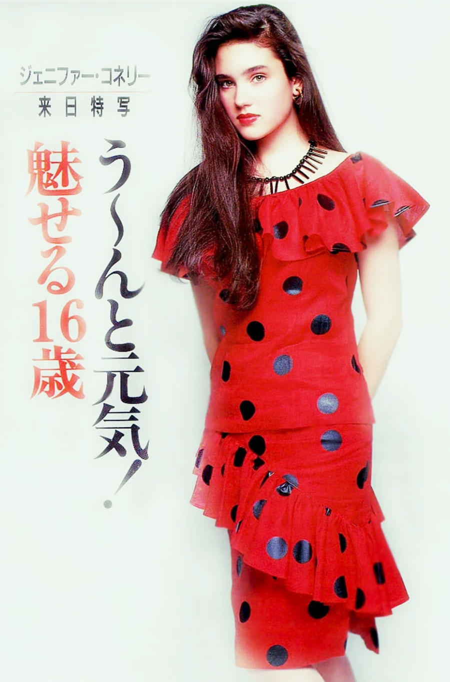 A young woman with long brown hair wears a red dress with black polka dots and ruffled sleeves, posing against a white background. Japanese text is written vertically and horizontally alongside her.