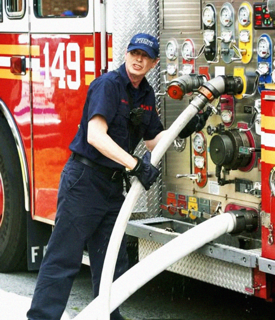 A firefighter in uniform connects large hoses to the side panel of a fire truck with multiple gauges and controls visible, preparing equipment for use. The truck is red and has the number 149 on it.