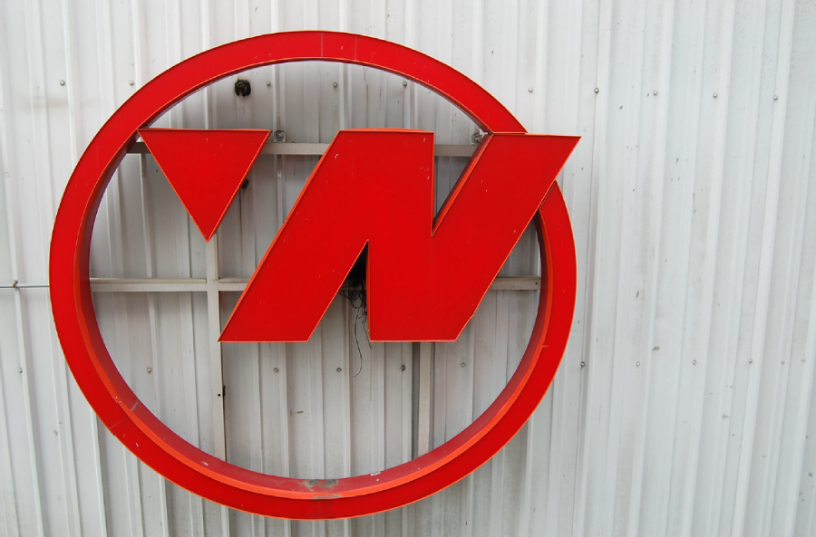 A large red "N" inside a red circle is mounted on a corrugated metal wall.