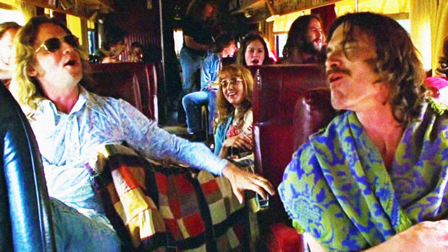 A group of people sing joyfully together while riding on a bus, with two men in the foreground enthusiastically singing. Sunlight streams through the windows, and others in the background appear to join in the fun.