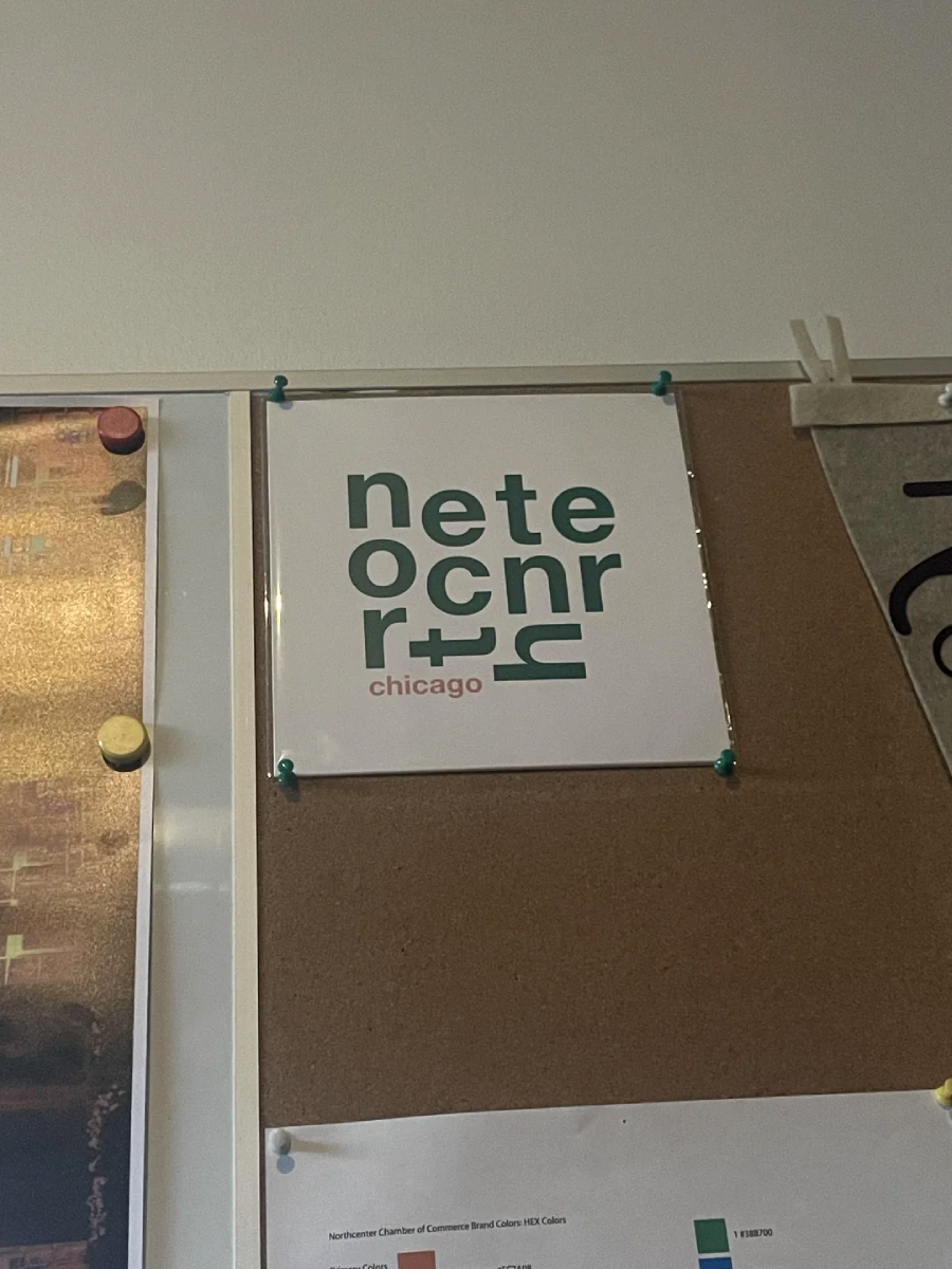 A square sign pinned to a corkboard displays the text "netecnrr+ chicago" in green and red, arranged in a modern, stacked layout with stylized letters.