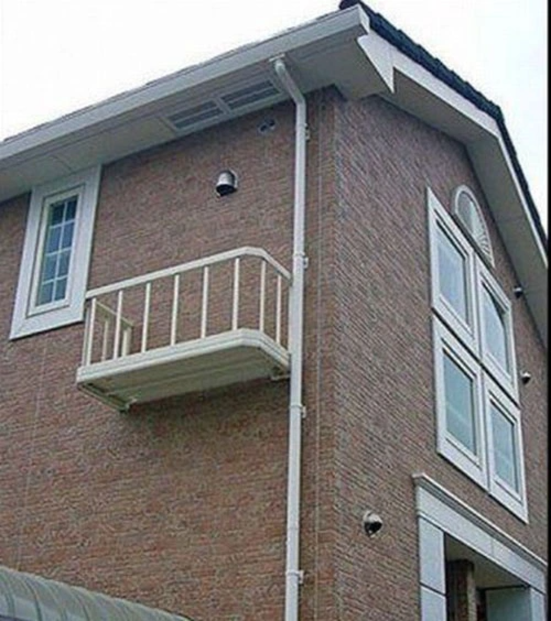A small balcony with a railing is attached to the side of a brick house, but there is no door or window providing access to it.