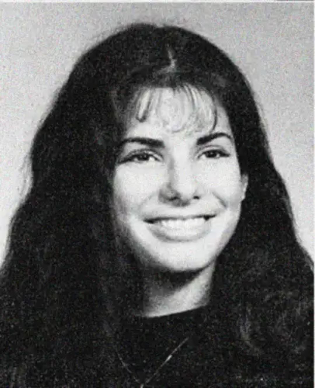 Black and white portrait of a young woman with long dark hair, smiling, wearing a dark top. The background is plain and light-colored.